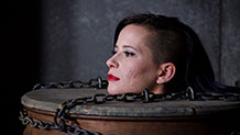 Freya French's head pokes out of metal drum bondage